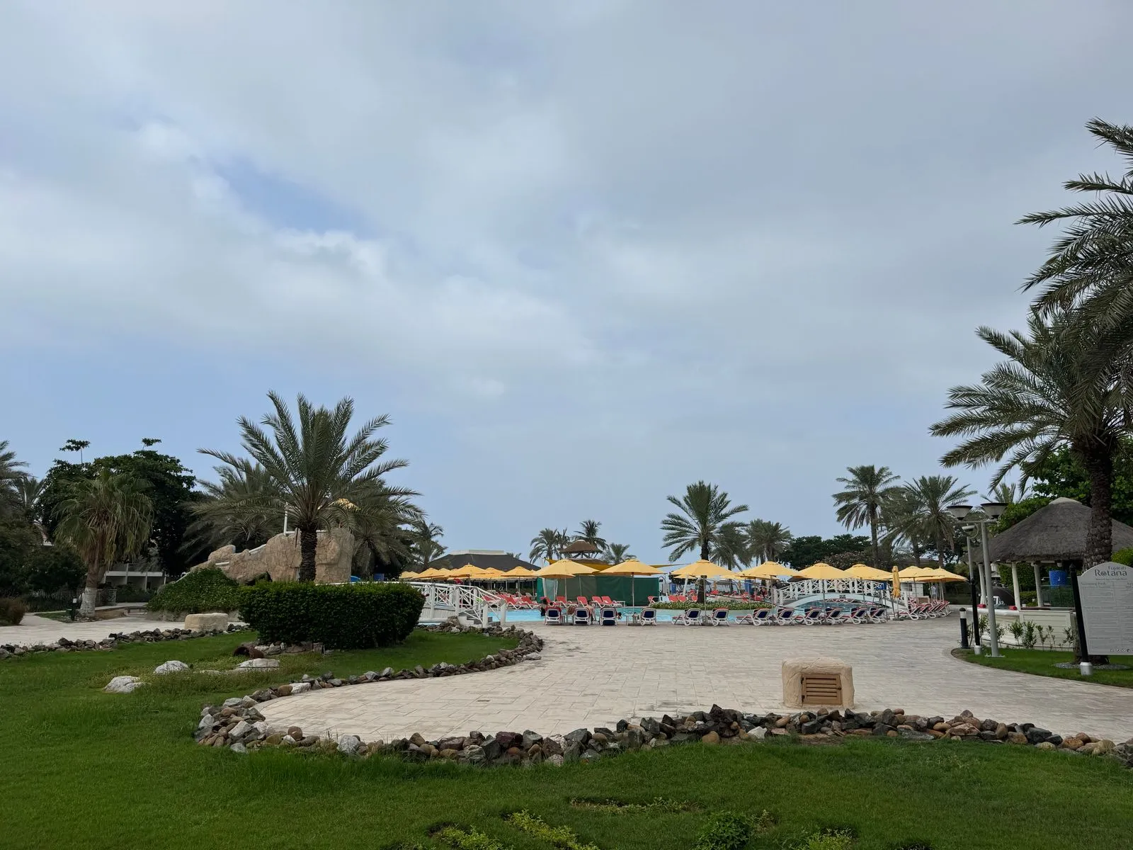Gartenanlage des Resorts mit Palmen, Poolbereich und Sonnenschirmen